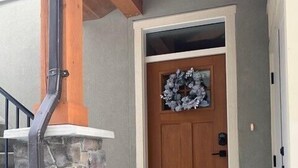 Una escalera de piedra que lleva a una puerta de madera adornada con un adorno, una barandilla metálica y un área de porche de hormigón.