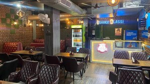 A restaurant interior with leather booths, tables, and a counter with a neon sign reading "SHAKE LASSI". - D 0101 Cafe and Lounge (Amritsar)