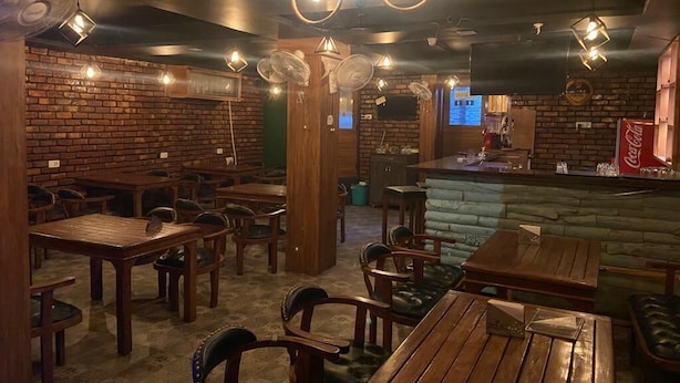 A restaurant with brick walls, wooden tables and chairs, and a bar area. - D 0101 Cafe and Lounge (Amritsar)