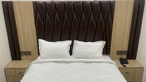 A neatly made bed with a quilted white duvet, two pillows, and a headboard with a dark brown, diamond-patterned design. - D 0101 Cafe and Lounge (Amritsar)