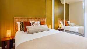 A neatly made bed with a patterned headboard, a bedside table with a lamp, and a large mirror on the wall. - Cascais Modern & Quiet Retreat (Cascais)