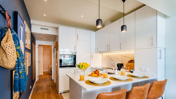 A modern kitchen with white cabinets, a central island with seating, and a hanging light fixture. - Cascais Modern & Quiet Retreat (Cascais)