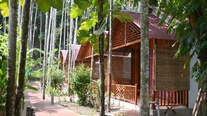 A pathway leading to a wooden building with a red roof, surrounded by tall trees and lush greenery. - Placid Garden Resort (Port Blair)