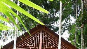 A wooden cabin with a geometric facade, a covered porch, and a view of the surrounding forest. - Placid Garden Resort (Port Blair)