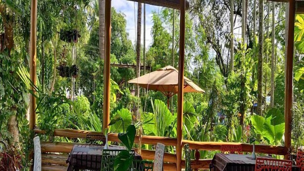 An outdoor patio with a wooden pergola, tables, chairs, and potted plants. - Placid Garden Resort (Port Blair)