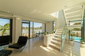 A modern interior with a glass staircase, a dining area with a view, and a pool outside.