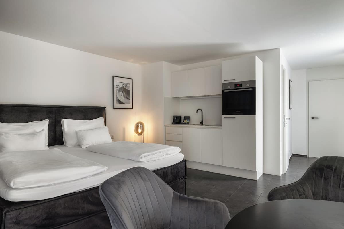 A modern hotel room with a large bed, a small kitchenette, and a dining area.