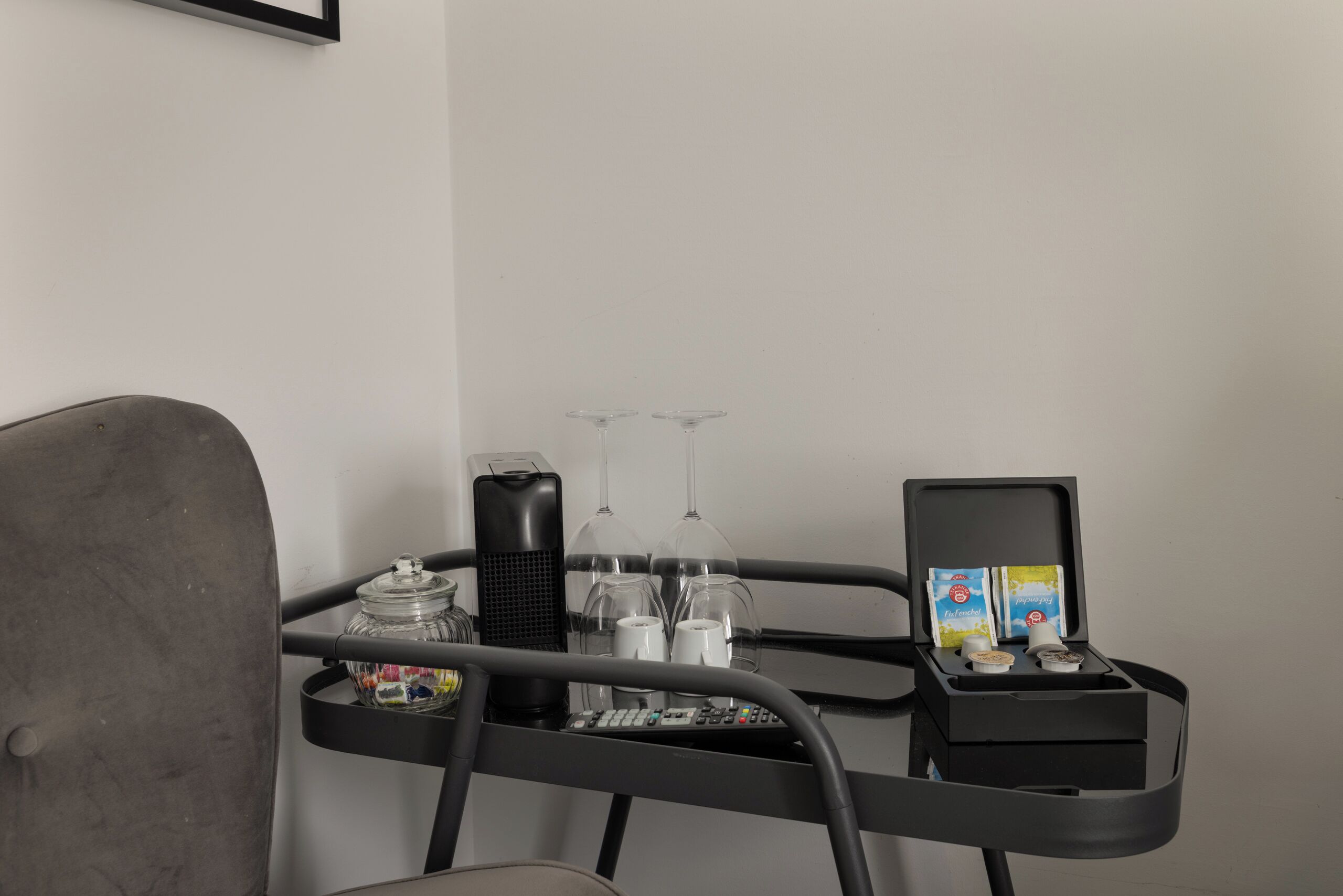 Une petite table avec une télécommande, un récipient en verre, deux verres à vin et une boîte de mouchoirs.