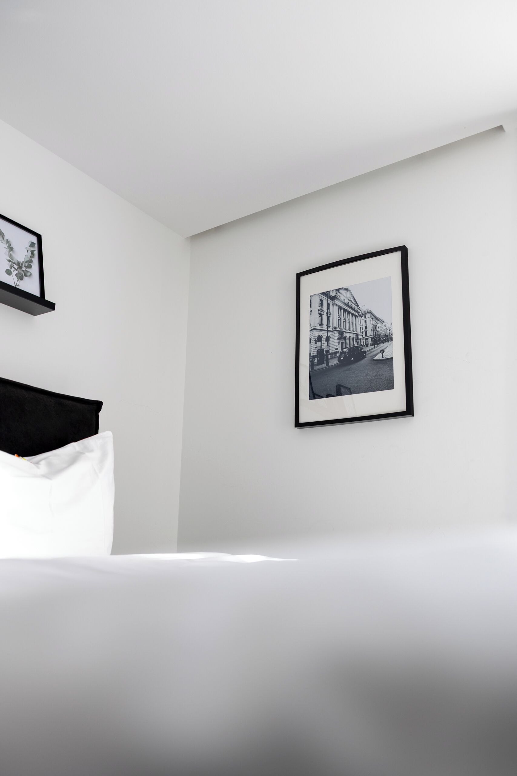 Habitación de hotel minimalista con una cama, una fotografía blanco y negro enmarcada en la pared y una pequeña estantería con un cuadro enmarcado.