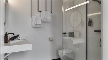 Un baño moderno con cabina de ducha de vidrio, un lavamanos blanco con dispensador de jabón y un inodoro.