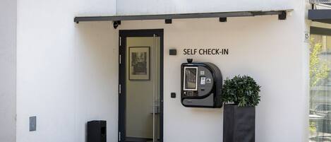 Un quiosco de auto-registro y una puerta con la leyenda 'SELF CHECK-IN' en una pared blanca.