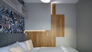 A modern bedroom with a grey upholstered headboard, a wooden accent wall, and a bed with white linens and rolled towels.