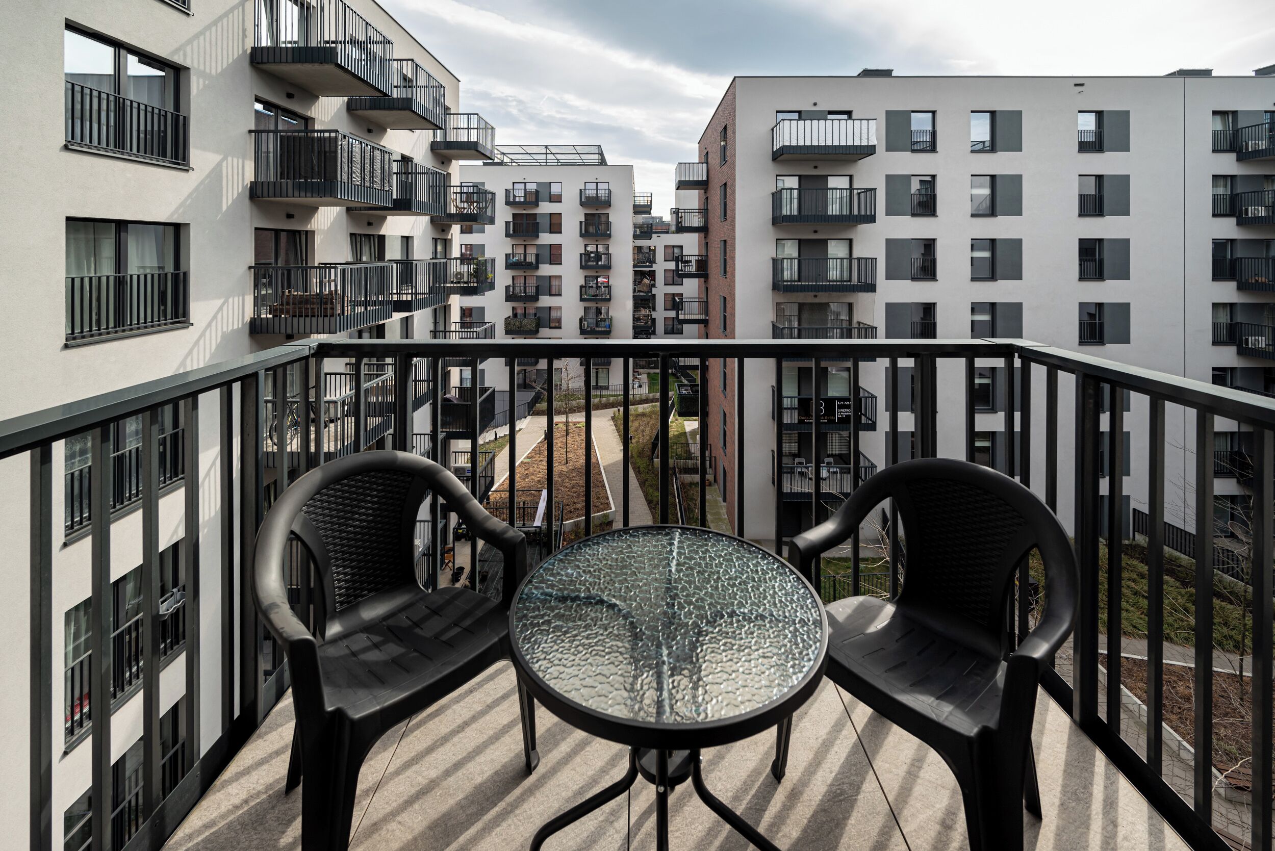 A balcony with two chairs and a table, overlooking a residential area with modern buildings.
