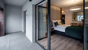 A modern bedroom with a sliding glass door leading to a balcony, a bed with a green quilt, and a bedside table with a lamp. - RentPlanet - Atal City Square (Wroclaw)
