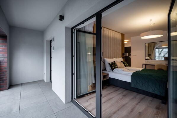 Un dormitorio moderno con puerta corrediza de vidrio que da a un balcón, una cama con colcha verde y una mesita de noche con lámpara.