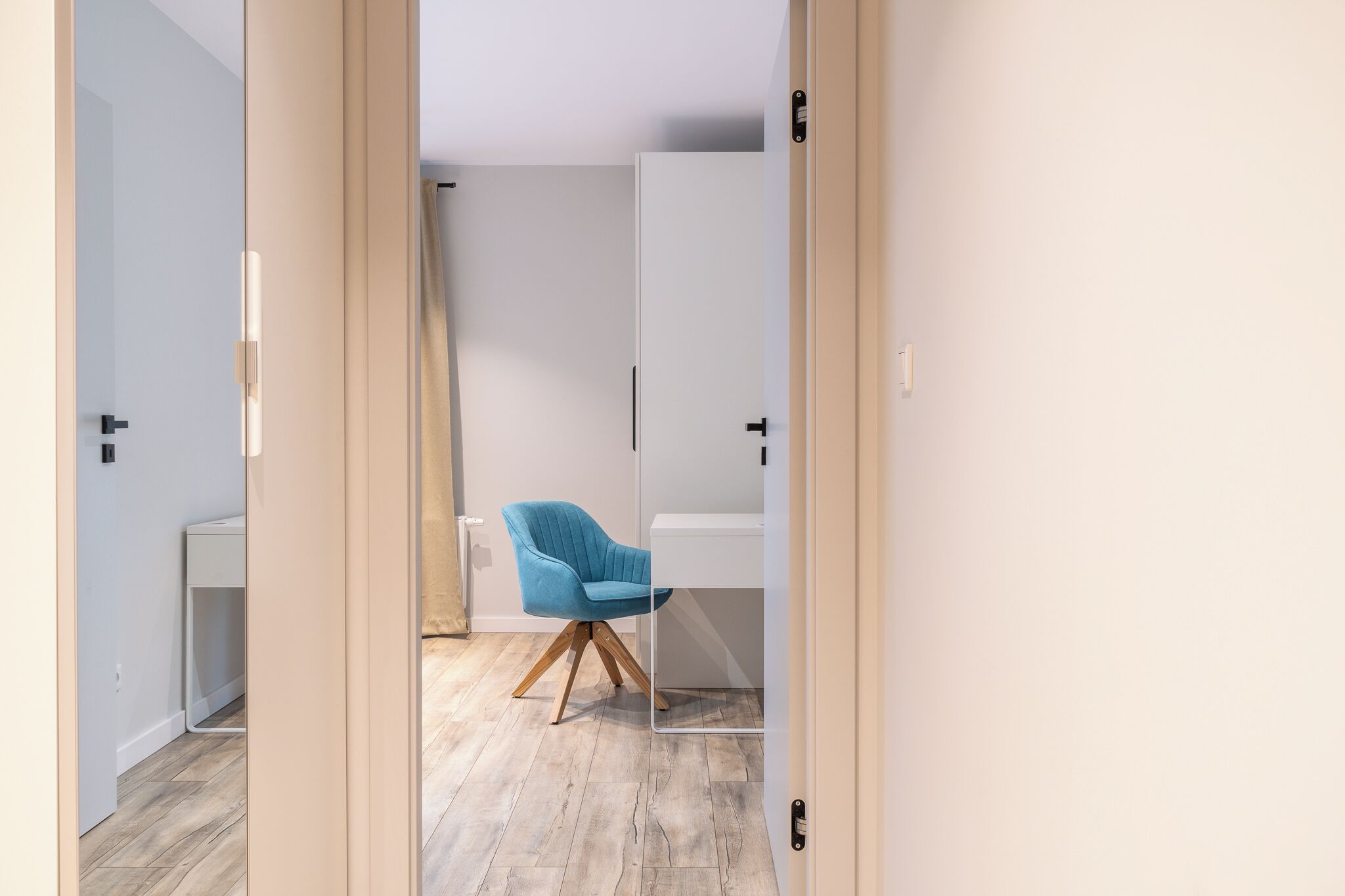 Une chambre moderne avec un plancher en bois, une chaise bleue et des meubles blancs.