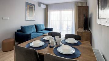 Un salon moderne avec une table à manger dressée pour six personnes, un canapé bleu et un téléviseur posé sur un meuble en bois.