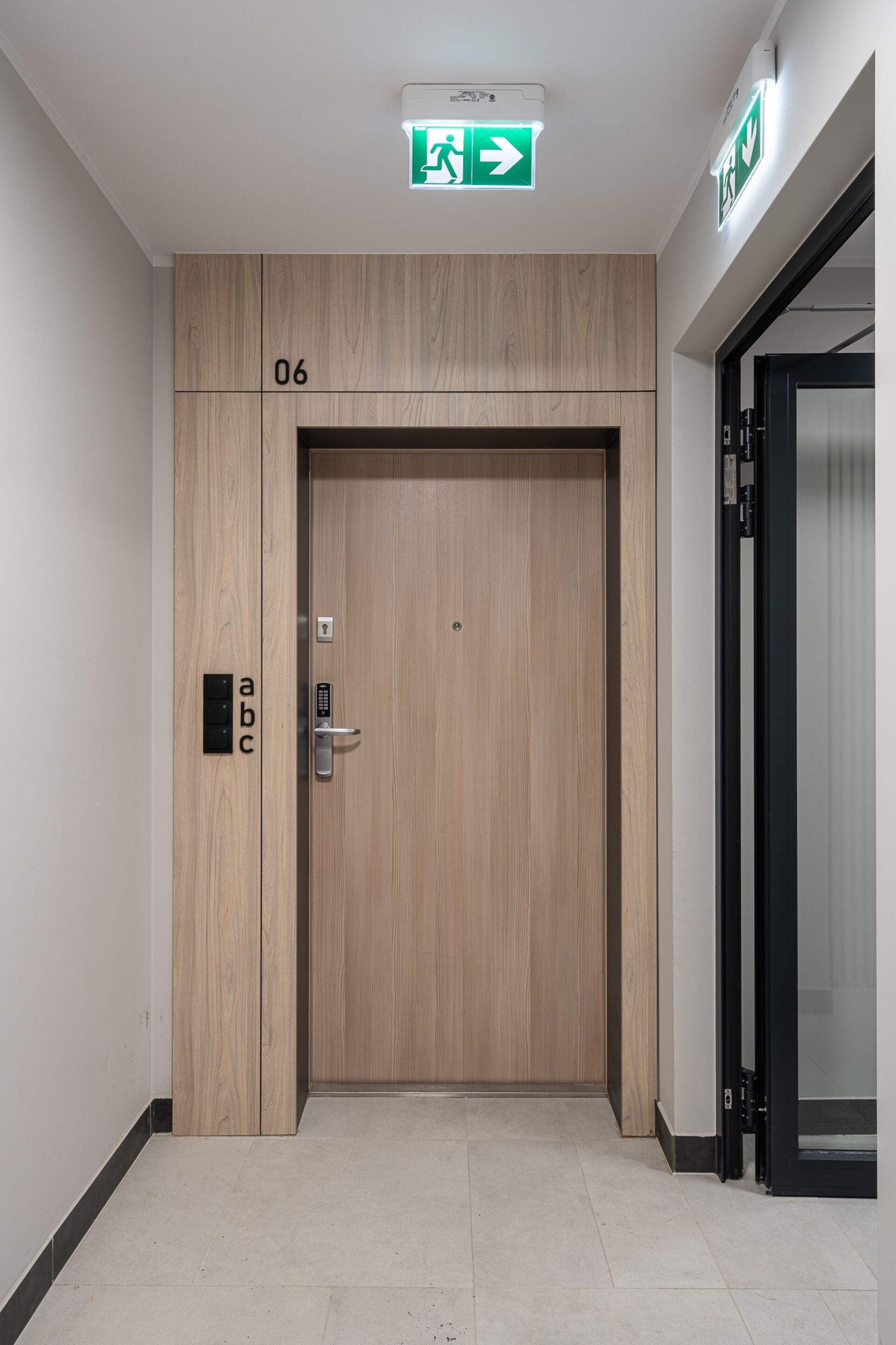 Una puerta de madera con cerradura electrónica, una señal de salida de emergencia verde encima y el número "06" en la pared.