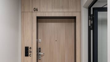 Una puerta de madera con cerradura electrónica, una señal de salida de emergencia verde encima y el número "06" en la pared.
