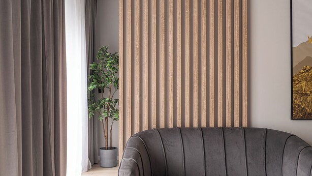 A modern living room with a grey sofa, a round coffee table with gold legs, a wooden slat wall panel, a potted plant, and a framed picture on the wall. - RentPlanet - Atal City Square (Wroclaw)
