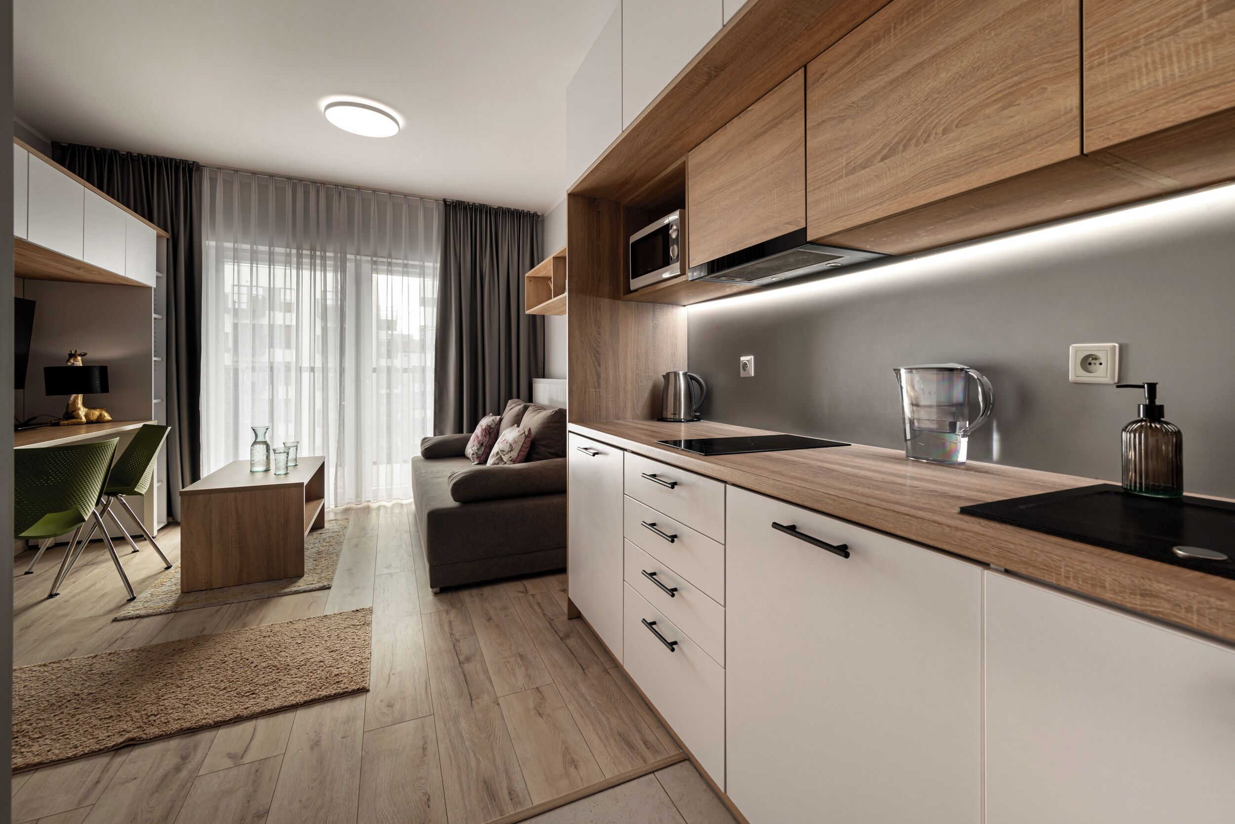 A modern kitchen with wooden cabinets, a built-in microwave, and a kettle.