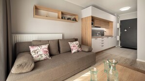 A modern living room with a sofa, a coffee table, and a kitchen area with cabinets and a countertop. - RentPlanet - Atal City Square (Wroclaw)