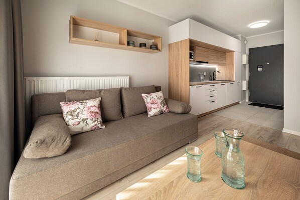 Ein modernes Wohnzimmer mit Sofa, Couchtisch und Küchenzeile mit Schränken und Arbeitsplatte.