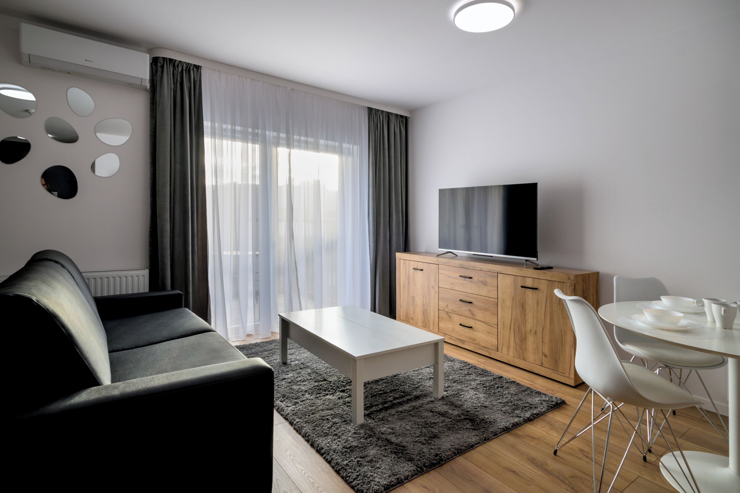 Een moderne woonkamer met een bank, een salontafel, een televisie op een houten kast, en een eethoek met stoelen en een tafel.