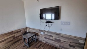 Una habitación con televisión montada en la pared, una mesita y una silla.