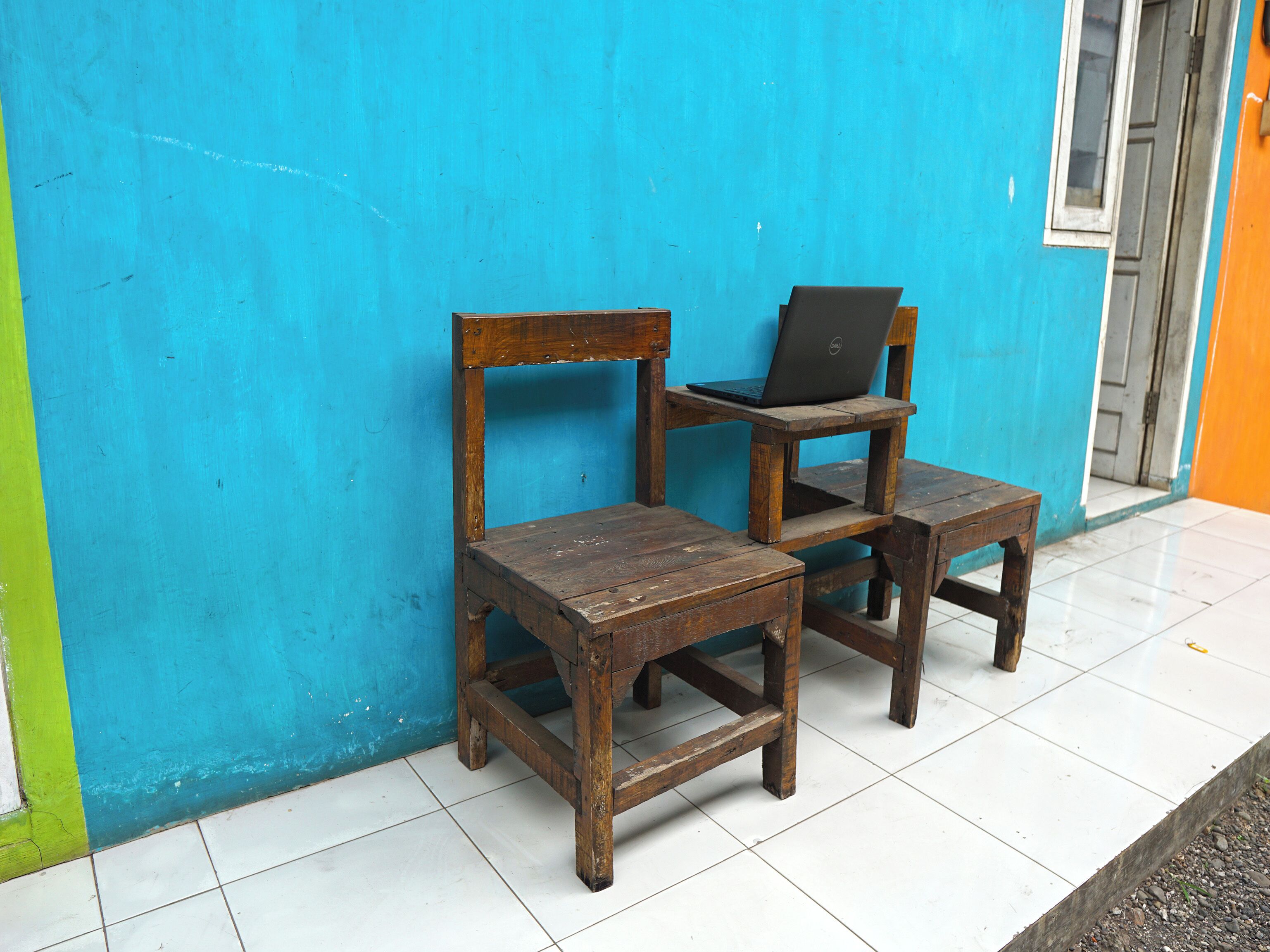Two wooden chairs with a laptop on one, positioned against a blue wall.