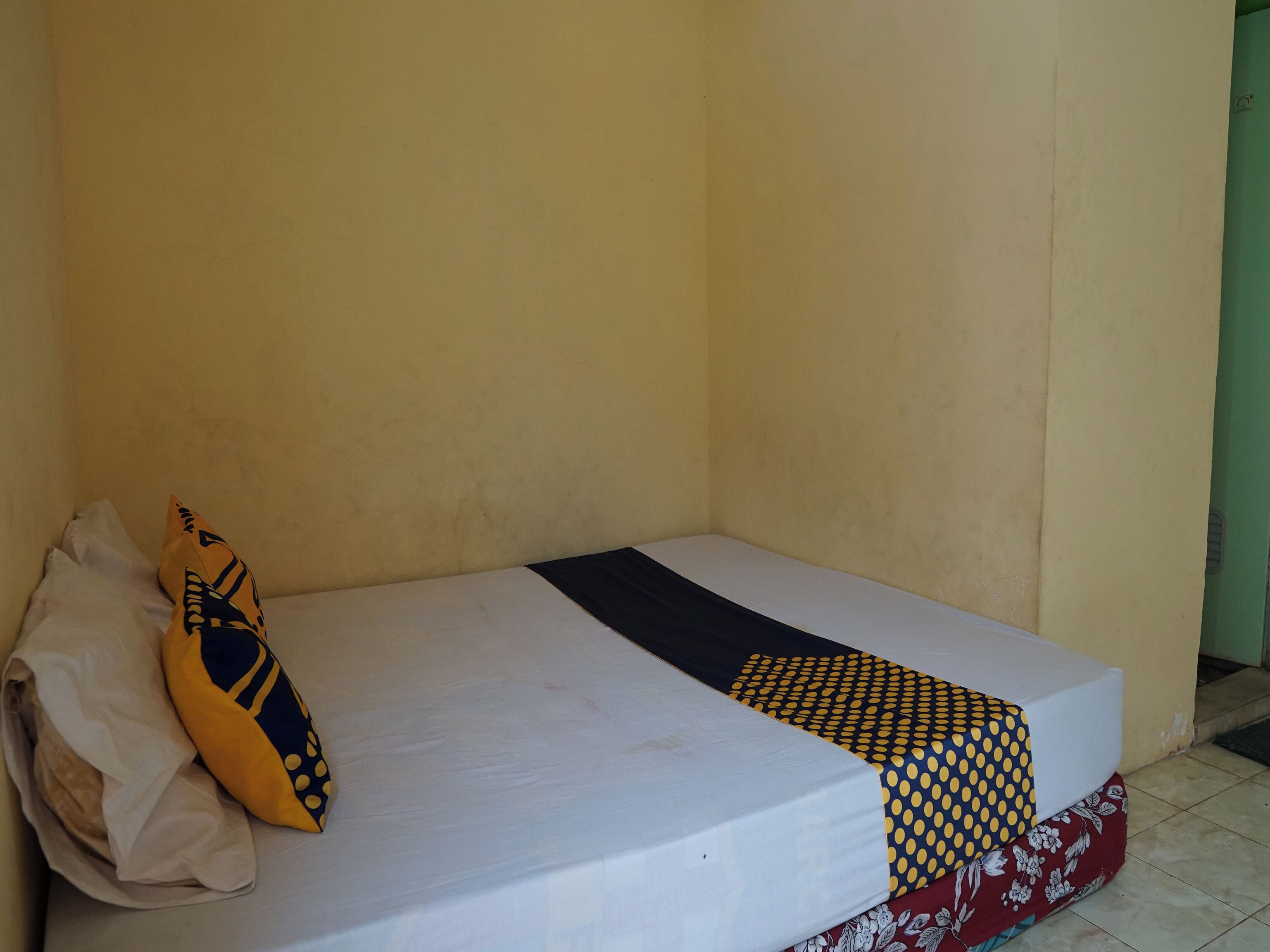 A single bed with a white mattress, a yellow pillow with a black design, and a patterned blanket.