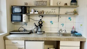 Une cuisine compacte équipée d’un four à micro-ondes, d’une machine à café et d’un évier. On y trouve des placards sous le plan de travail et une poubelle en dessous.