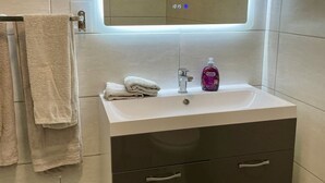 Une salle de bain moderne avec un lavabo blanc, un miroir doté d’un éclairage sous le meuble, des toilettes et une poubelle.