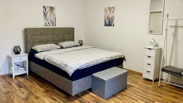 Une chambre à coucher comprenant un lit, des tables de chevet, un banc, une commode et un miroir.