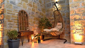 A stone-walled room with a hanging chair, a wooden table, and potted plants. - Maslin Otel (Gökçeada)