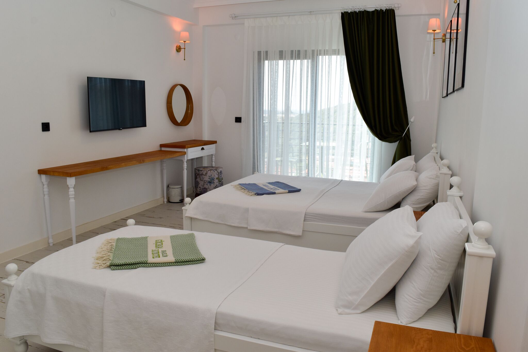 A hotel room with two beds, a TV, a small table, and a window with curtains.