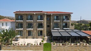 A multi-story building with stone facade, balconies, and a covered outdoor seating area with potted plants. - Maslin Otel (Gökçeada)