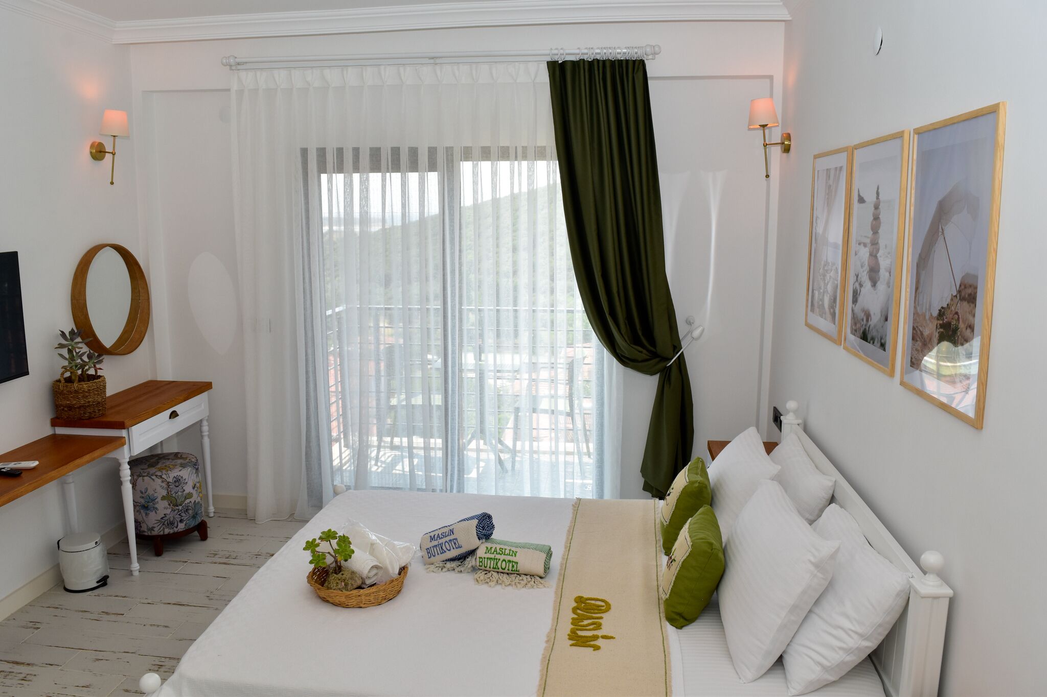 A hotel room with a bed, a desk, a chair, a window with curtains, and framed pictures on the wall.