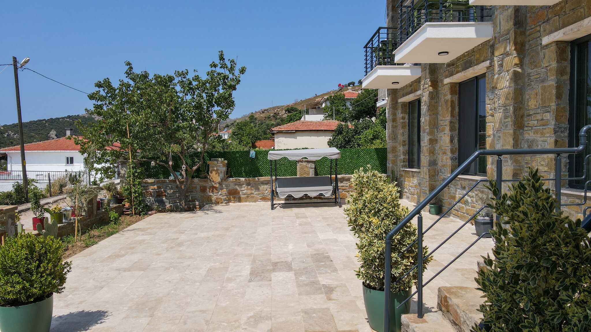 A courtyard with a stone floor, a pergola, and potted plants.