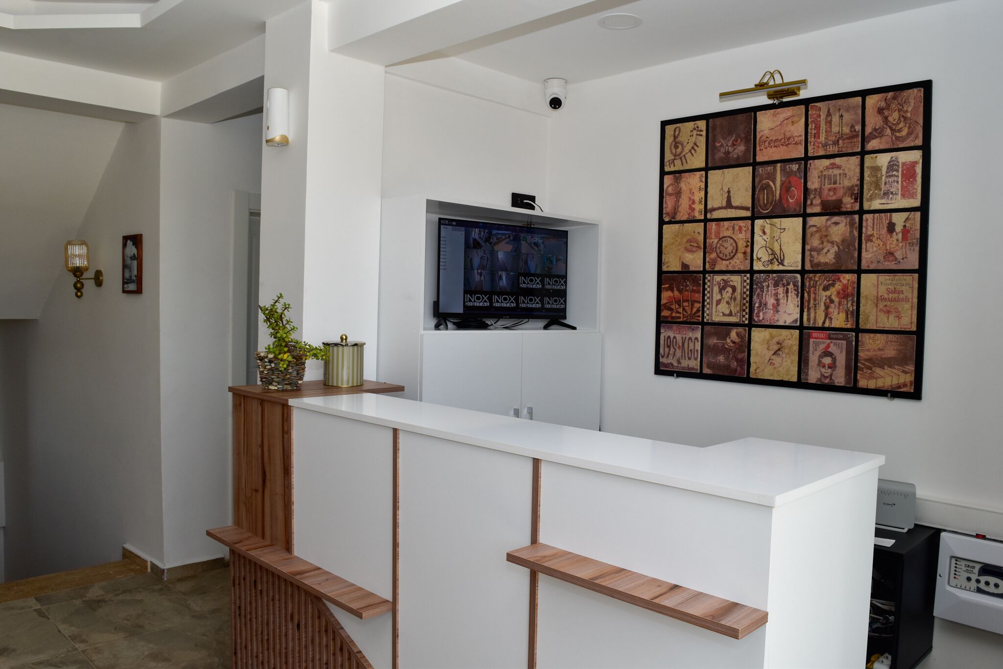 A reception area with a white counter, wooden shelves, a mounted television, and a collage of vintage posters on the wall.