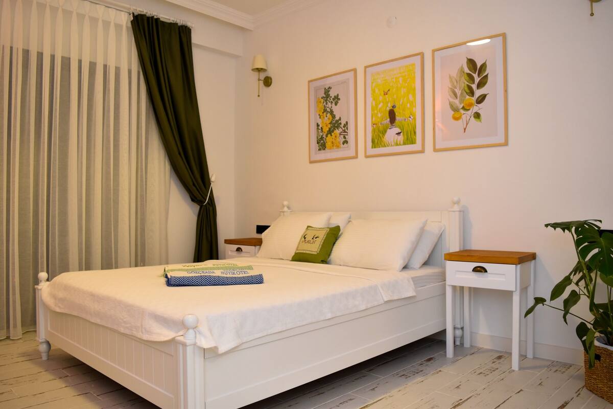 A white bed with a green pillow, a bedside table, and a plant.