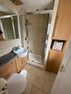 A bathroom with a shower, sink, toilet, and wooden cabinets. - 2BD Flat With Views of Canary Wharf - Rotherhithe (London)