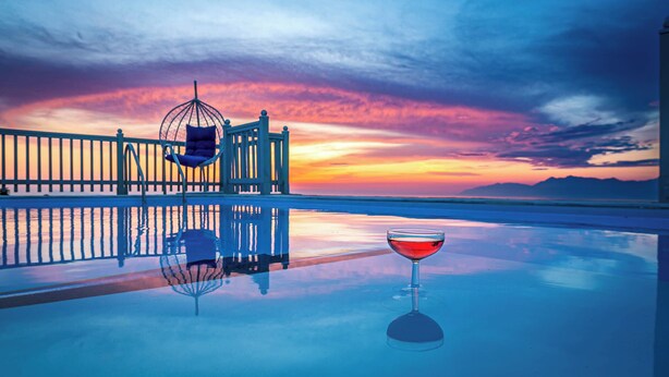 A sunset view from a balcony with a glass table, a glass of red wine, and a hammock. - Villa Orizontas Corfu, Private Villa With Breathtaking Views (Corfu)