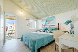 A bedroom with a bed, a table, and a chair. There is a window and a door leading to an outdoor area.