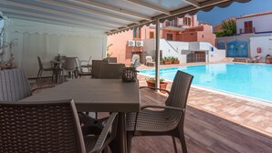 A covered outdoor area with a pool, wicker furniture, and a view of nearby buildings.