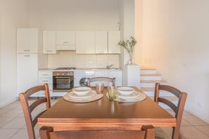 Comedor con una mesa de madera dispuesta para cuatro, una cocina al fondo y una escalera que sube a un nivel superior.