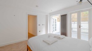 Une chambre à coucher moderne avec un grand lit, une porte donnant sur un balcon et un luminaire au plafond.