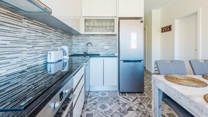 Una cocina compacta con diseño moderno, que incluye un refrigerador de acero inoxidable, un microondas y un horno empotrado. La cocina tiene un salpicadero de azulejos y un piso estampado.
