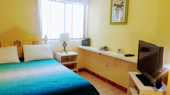 A hotel room with a bed, a television, a nightstand, a lamp, and a window with blinds.