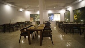 Un comedor amplio con mesas y sillas largas, ventiladores de techo y ventanas grandes que dejan entrar luz natural.